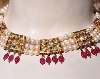 May include: A gold choker necklace with three strands of white pearls and square-shaped pendants set with clear stones. The pendants are accented with dangling ruby red beads.