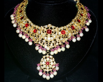 May include: A gold necklace with a large, ornate pendant. The necklace is decorated with red and white gemstones and pearls.