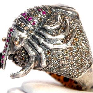 Pode incluir: Um anel de prata com um design de escorpião detalhado. O escorpião é coberto com pequenos diamantes brilhantes e rubis vermelhos.