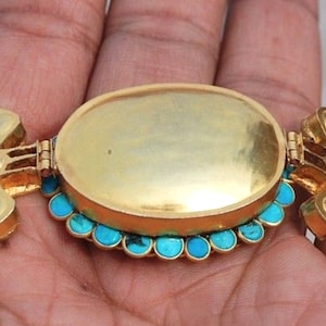 Puede incluir: Un collar de oro con un colgante ovalado de turquesa y oro. El colgante est&aacute; abierto y el interior est&aacute; vac&iacute;o. El collar est&aacute; hecho de perlas blancas y cuentas de turquesa.