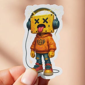 May include: A sticker featuring a cartoon character with a yellow box head, black headphones, and a tongue sticking out. The character wears an orange hoodie, blue jeans, and red sneakers. The sticker is held by a hand.
