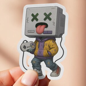 May include: A sticker featuring a cartoon character with a retro TV head, crossed-out eyes, and a sticking-out tongue. The character wears a yellow jacket, blue jeans, and holds a video game controller.