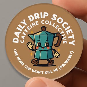 Op de afbeelding: Een ronde, bruine sticker met de tekst "Daily Drip Society Caffeine Collective" en een cartoon koffiezetapparaat. Het koffiezetapparaat is turquoise met een bruin handvat en lacht. De tekst "One More Cup Won't Kill Me (Probably)" staat ook op de sticker.