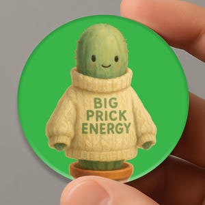 May include: A round, green button featuring a cartoon cactus wearing a beige sweater. The sweater has the text "BIG PRICK ENERGY" printed on it. The cactus is in a brown pot, set against a bright green background.