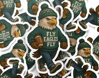 Op de afbeelding: Een sticker met een adelaarsmascotte die een groene trui en muts draagt en een voetbal vasthoudt. De tekst "FLY EAGLES FLY" staat op de trui. De adelaar wordt afgebeeld in een wandelhouding, met een blauwe spijkerbroek en sneakers.