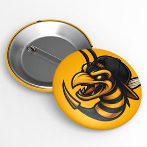 May include: A yellow button pin featuring a cartoon illustration of an angry-looking bee wearing a black cap. The bee has yellow and black stripes, a sharp beak, and a menacing expression. The pin's back is silver.