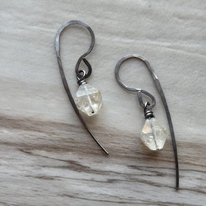 May include: A pair of silver earrings with a clear, faceted gemstone hanging from each. The earrings are made of thin, wire-like metal.