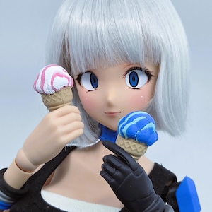 May include: A doll with short white hair and large blue eyes holding two miniature ice cream cones. One cone features pink and white swirls, while the other has blue and light blue swirls. The doll wears a black top with a white trim and blue arm armor.