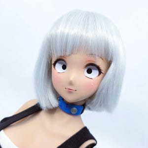 May include: A doll head with short, straight, silver-white hair and a blunt fringe. The face features large, wide-set white eyes with black pupils, a small nose, and a subtle smile. A blue collar with a circular silver accent is worn around the neck.