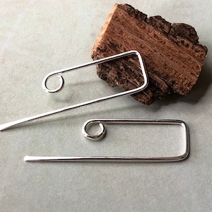 May include: A pair of silver earrings with a simple, geometric design. Each earring features a thin, rectangular shape with a small circle at one end.