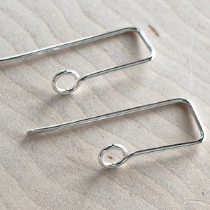 May include: A pair of silver earring hooks with a square shape and a small loop at the end.