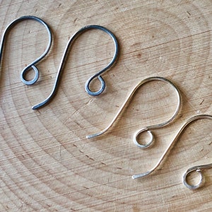 May include: Four silver earring hooks, two are silver and two are black, on a wooden surface.