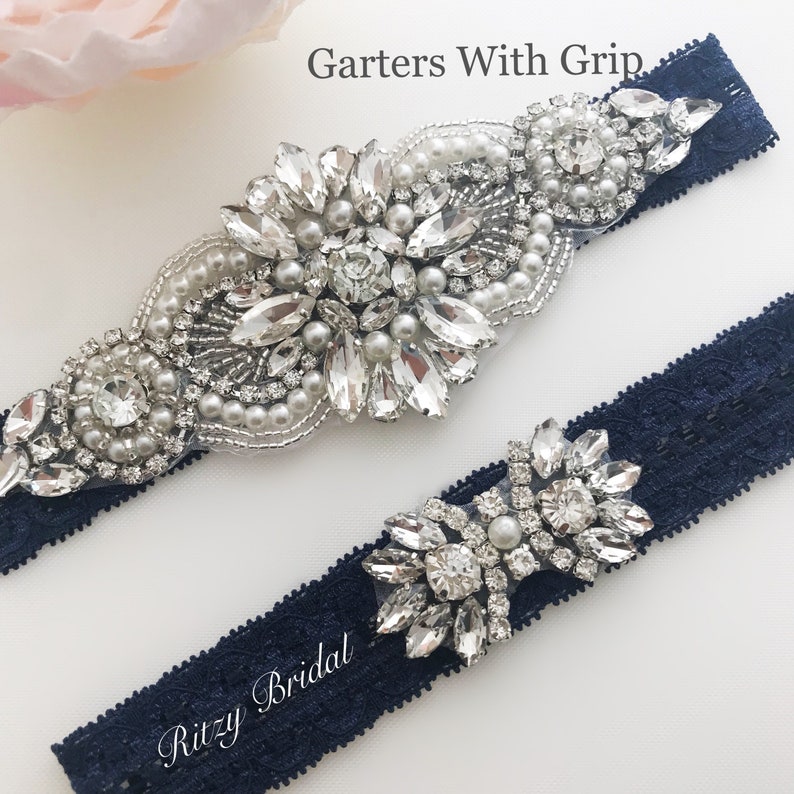 The image showcases a stunning silver wedding garter on a navy lace background, creating a captivating contrast. The garter is beautifully adorned with rhinestone embellishments, adding a touch of glamour and elegance to the design.