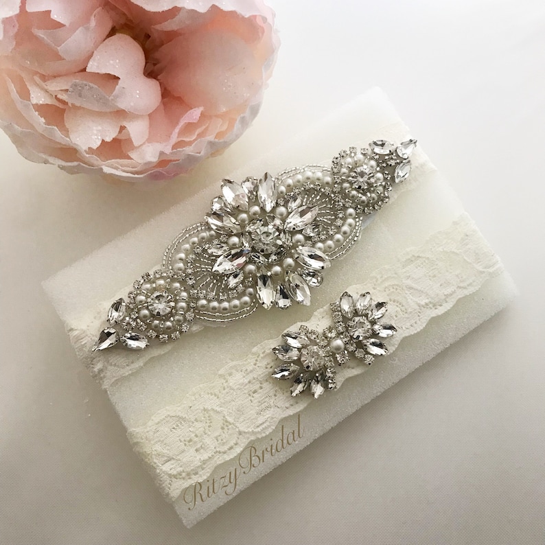 The lace band of the garter exhibits a delicate floral pattern, exuding elegance and charm. The rhinestone embellishments are strategically placed along the lace, catching the light and creating a dazzling effect.