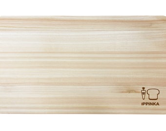 May include: A light wood cutting board with a natural grain pattern. The board has a small logo of a carrot and a loaf of bread with the text "IPPINKA" underneath.