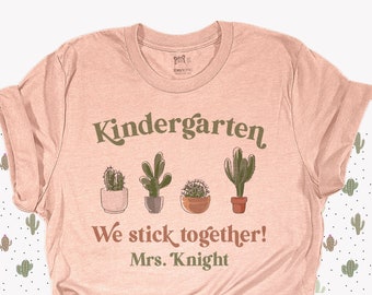 May include: A pink t-shirt with the text "Kindergarten We stick together! Mrs. Knight" and a row of four potted cactus plants.
