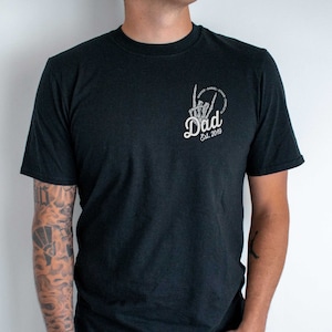 Peut inclure: T-shirt noir avec un graphique blanc d'une main squelettique faisant un signe de paix avec le texte "Dad Est. 2019" autour.
