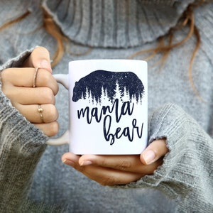 May include: White ceramic mug with a black silhouette of a bear in a forest with the text "mama bear" printed on the front.