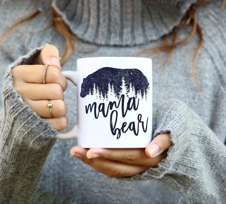 May include: White ceramic mug with a black silhouette of a bear in a forest with the text "mama bear" printed on the front.