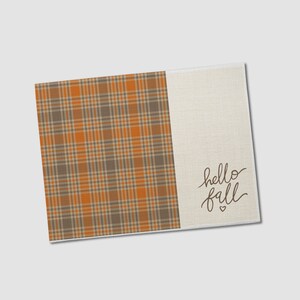 May include: A rectangular kitchen towel with a plaid pattern in shades of brown, orange, and tan. The right side is a solid tan color with the words "hello fall" in a script font and a small heart.
