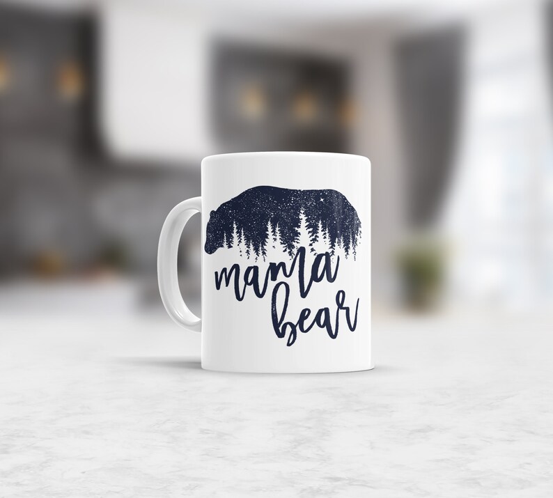 May include: White ceramic mug with a black silhouette of a bear with trees inside the bear. The text "mama bear" is written below the bear.