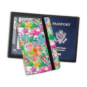 May include: A black passport holder with a pink flamingo and floral print. The holder has a clear plastic window for a boarding pass and a black elastic band to secure the passport.