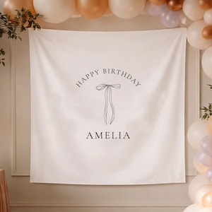 Può includere: Un banner bianco con la scritta "Happy Birthday Amelia" e un'illustrazione di scarpette da ballo. Il banner è circondato da palloncini bianchi, pesca e oro, creando un'atmosfera festosa. Il verde aggiunge un tocco naturale.