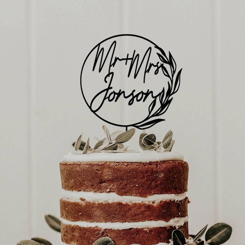 May include: Black and white cake topper with the text "Mr & Mrs Johnson" in a circle with a leafy design.