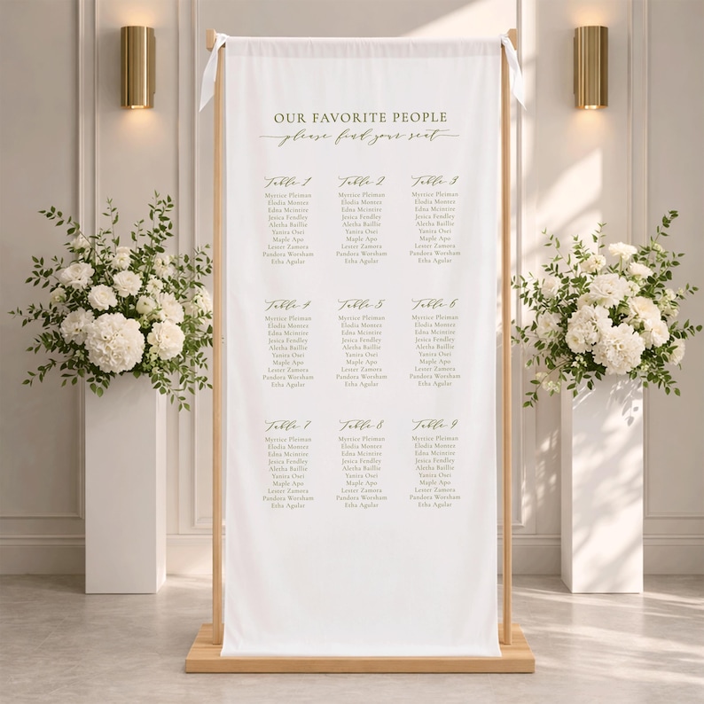 Pu&ograve; includere: Un cartello in tessuto bianco per il tableau de mariage, sospeso su un supporto in legno chiaro. Il cartello presenta il testo "OUR FAVORITE PEOPLE" e "please find your seat" in lettere dorate, seguito da nove tavoli con elenchi di nomi in grigio scuro.