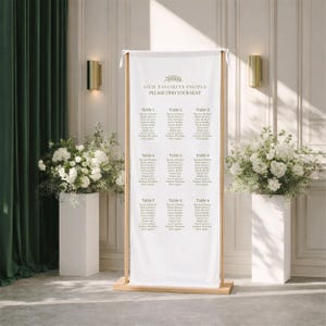 Pu&ograve; includere: Un alto cartello rettangolare per il tableau de mariage in tessuto bianco, sospeso a una cornice in legno chiaro. Il cartello riporta il testo "OUR FAVORITE PEOPLE" e "PLEASE FIND YOUR SEAT" sopra un elenco di nove tavoli con nomi in grigio scuro.
