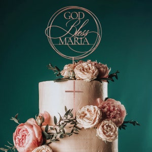 Peut inclure: Un g&acirc;teau de mariage &agrave; deux &eacute;tages d&eacute;cor&eacute; de roses roses et de verdure. Un dessus de g&acirc;teau avec les mots "God Bless Maria" est plac&eacute; sur le dessus du g&acirc;teau.
