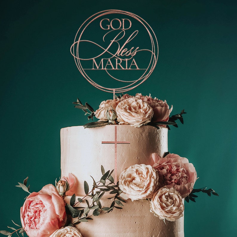Peut inclure: Un g&acirc;teau de mariage &agrave; deux &eacute;tages d&eacute;cor&eacute; de roses roses et de verdure. Un dessus de g&acirc;teau avec les mots "God Bless Maria" est plac&eacute; sur le dessus du g&acirc;teau.
