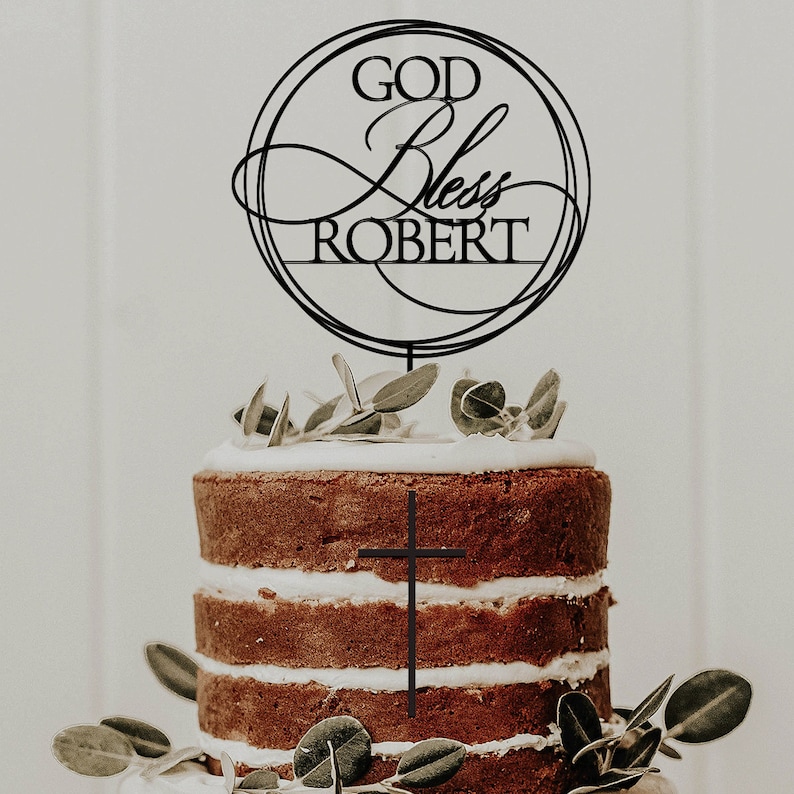 Peut inclure: Un topper de g&acirc;teau noir avec le texte "God Bless Robert" dans un cercle avec une croix sur un g&acirc;teau.
