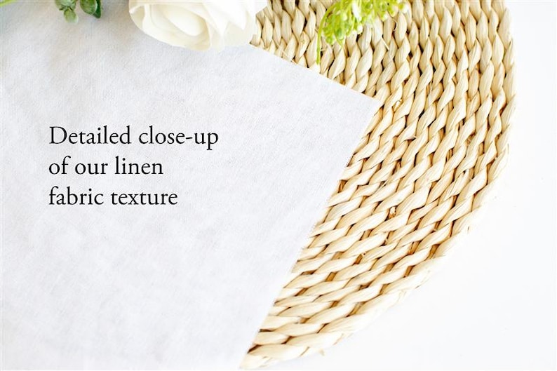 May include: A close-up of white linen fabric with the text "Detailed close-up of our linen fabric texture". The fabric is partially covering a woven, circular placemat. A white flower and greenery are in the background.