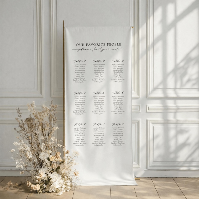 Pu&ograve; includere: Un alto cartello verticale bianco per il tableau de mariage con il testo "OUR FAVORITE PEOPLE" e "find your seat" seguito da un elenco di nove tavoli con i nomi degli ospiti stampati in inchiostro nero, su un supporto in metallo dorato.