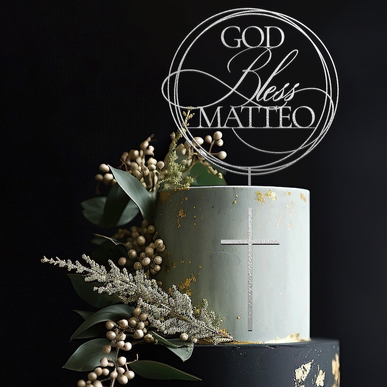 Peut inclure: Un g&acirc;teau &agrave; deux &eacute;tages d&eacute;cor&eacute; d'une croix argent&eacute;e et d'un dessus argent&eacute; qui dit "GOD Bless MATTEO". Le g&acirc;teau est glac&eacute; d'une couleur bleu clair avec des paillettes dor&eacute;es et est entour&eacute; de verdure.