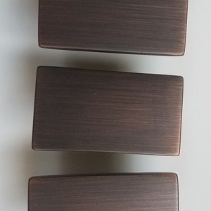 May include: Three rectangular cabinet pulls in a brushed bronze finish.