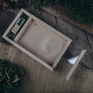 May include: A wooden box with a lid, engraved with a wreath and the initials "K & I" and the date "October 27th, 2023". The box contains a small wooden USB drive with the text "K&I Memories" engraved on it.