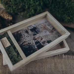May include: A wooden box with a glass top, containing a photo of a couple and a small wooden plaque with the text "K&L 10.14.23". The box is sitting on a burlap surface.