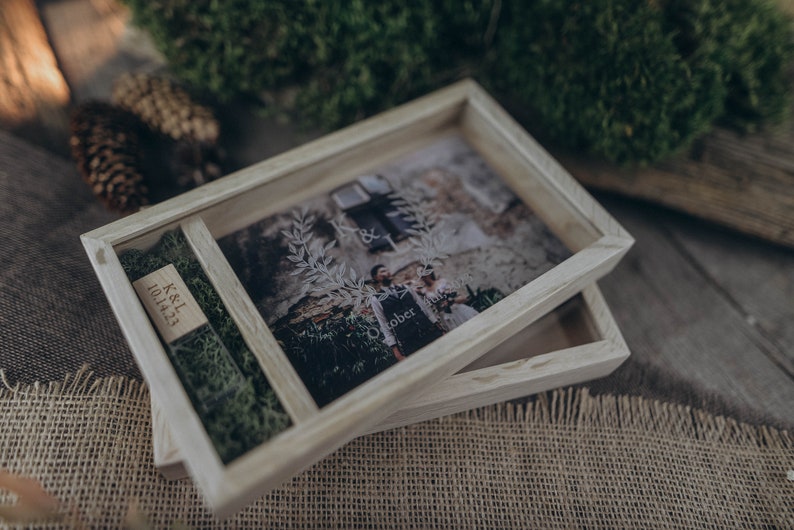 May include: A wooden box with a glass top, containing a photo of a couple and a small wooden plaque with the text "K&L 10.14.23". The box is sitting on a burlap surface.