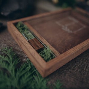 May include: A wooden box with a glass insert, containing a small wooden USB drive and green moss. The box is sitting on a brown burlap surface.