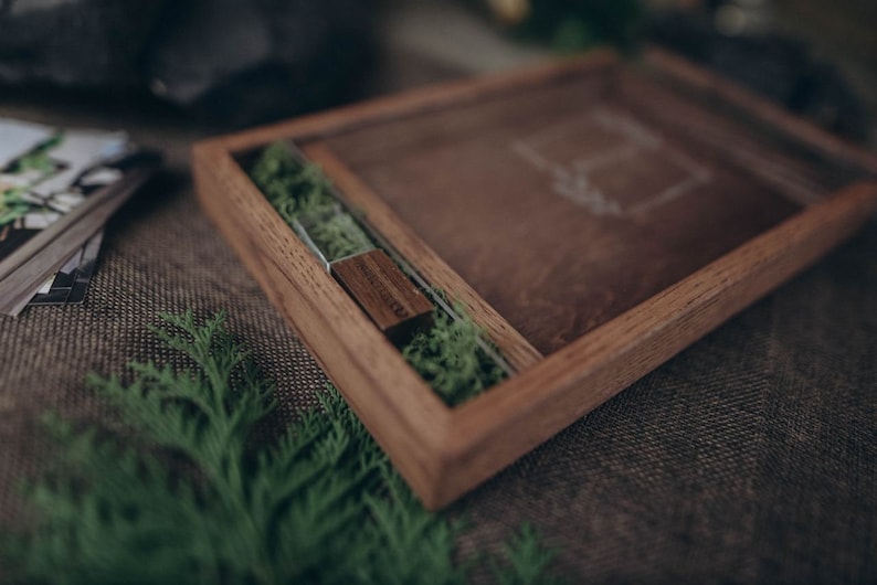 May include: A wooden box with a glass insert, containing a small wooden USB drive and green moss. The box is sitting on a brown burlap surface.