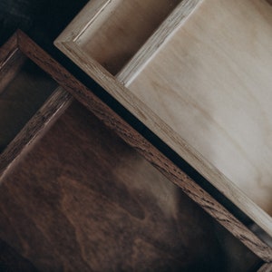 May include: Two wooden boxes with glass lids. The top box is light brown and the bottom box is dark brown.