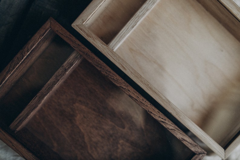 May include: Two wooden boxes with glass lids. The top box is light brown and the bottom box is dark brown.