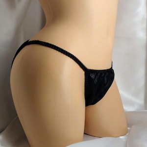 Może przedstawiać: Czarna satynowa bielizna z niskim stanem i cienkimi ramiączkami.