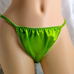 May include: Bright green satin thong underwear with white lace trim. The lingerie features a delicate string design and is made of a shiny, smooth fabric. The edges are finished with a contrasting white trim.