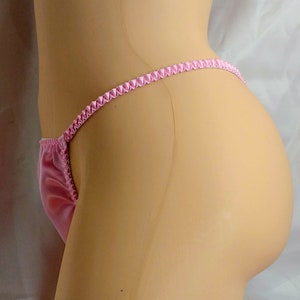 May include: Pink satin lingerie with a ruffled trim. The lingerie is shown on a mannequin.