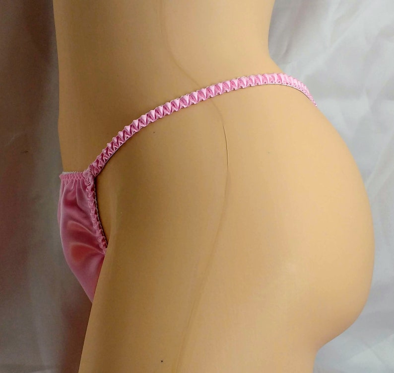 May include: Pink satin lingerie with a ruffled trim. The lingerie is shown on a mannequin.
