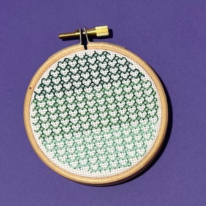 May include: A green and white embroidery hoop with a pattern of hearts. The hearts are arranged in a gradient pattern, with the darkest green hearts at the bottom and the lightest green hearts at the top.