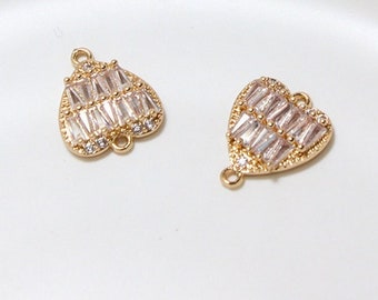 May include: Two gold-colored heart-shaped charms. Each charm is encrusted with rectangular, clear crystals. The charms have small loops at the top and bottom for attaching to jewelry. The background is a white surface.